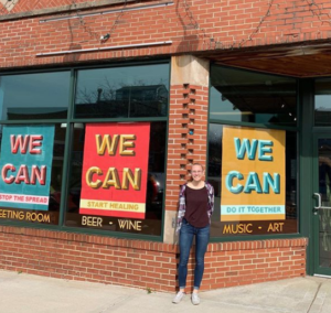 Maddie LeBrun '20 stands outside a shop in Oregon, WI that displays her posters in the windows.